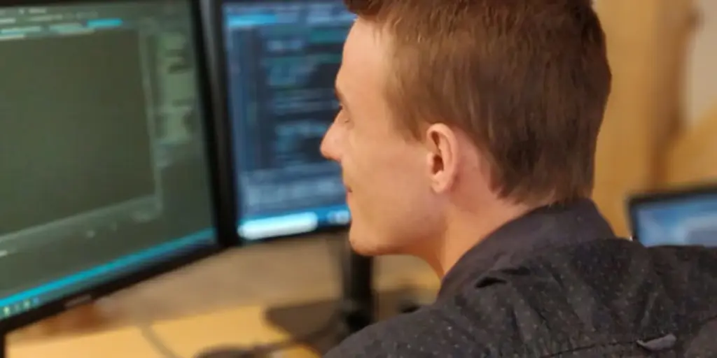 Mand arbejder ved computer med kode på skærme